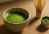 Frothy ceremonial matcha tea in a ceramic chawan bowl with bamboo whisk and matcha powder tin