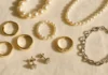 Flat lay of gold rings, pearl necklaces and diamond earrings arranged as jewellery gifting options on ivory linen