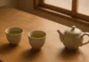 Two ceramic cups of green tea on a wooden table in soft morning light illustrating mindful tea drinking