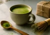 Vibrant green matcha latte in ceramic cup with bamboo whisk and ceremonial matcha gift tin on marble surface