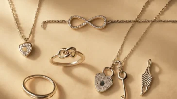 Romantiškų papuošalų simbolių vaizdas iš viršaus: širdies pakabukas, begalybės apyrankė ir meilės mazgo žiedas ant lino audinio