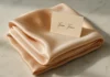 A folded silk scarf in peach tones with a gift card on white marble surface