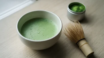 Keraminis dubuo su ryškiai žaliu matcha latte ir bambukiniu šluotele, iliustruojantis pagrindines matcha teikiamas naudas