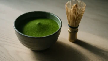 Ryškiai žalios spalvos ceremoninis matcha milteliai keraminiame dubenyje su bambukiniu šluotele ant medinės površės