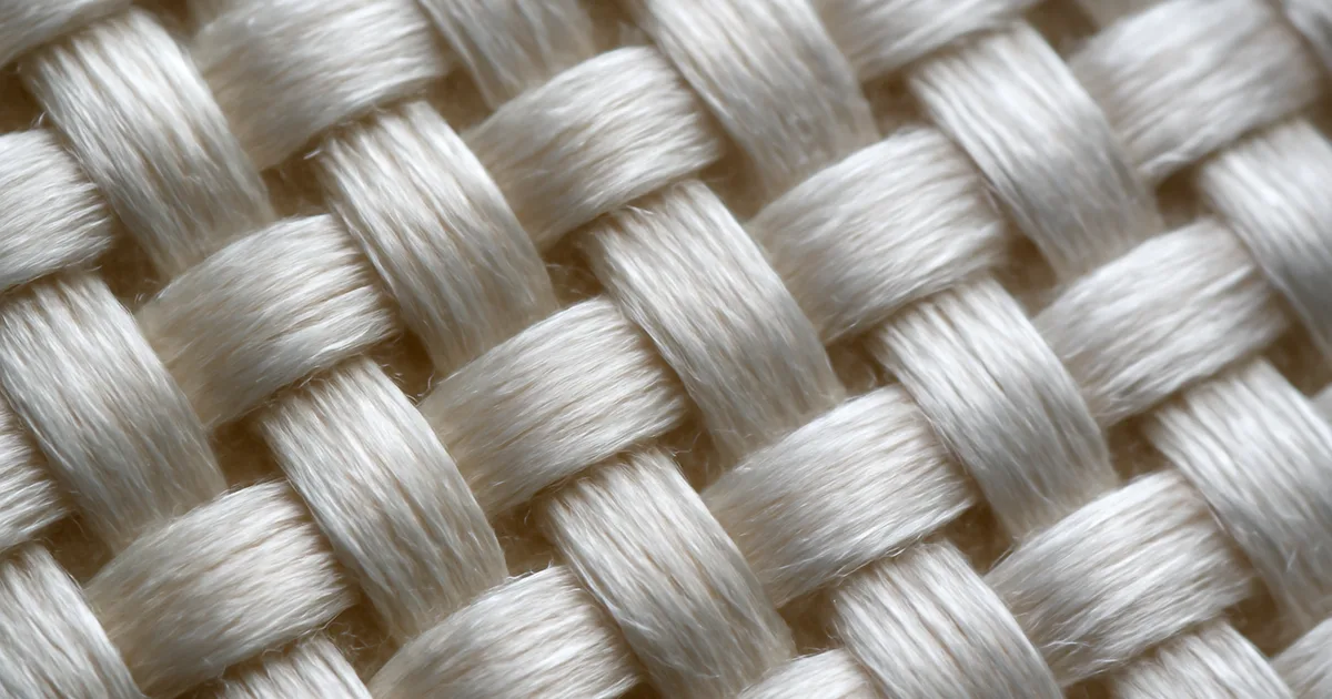 Iš arti nufotografuotas šilkinio šaliko audinys, atskleidžiantis natūralių skaidulų struktūrą ir žvilgantį blizgesį