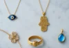 Simbolinių papuošalų kompozicija su piktąja akimi, hamsa, Claddagh žiedu ir gimimo akmens pakabuku ant marmuro
